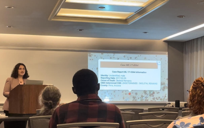 Student Haley Planicka standing at a classroom podium next to a slideshow presentation of her research